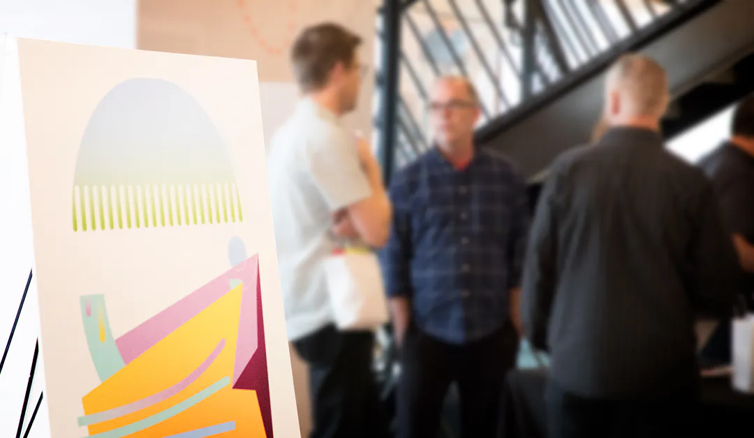 A custom art print with bright orange and pink color displayed with two men standing and talking to each other behind it.