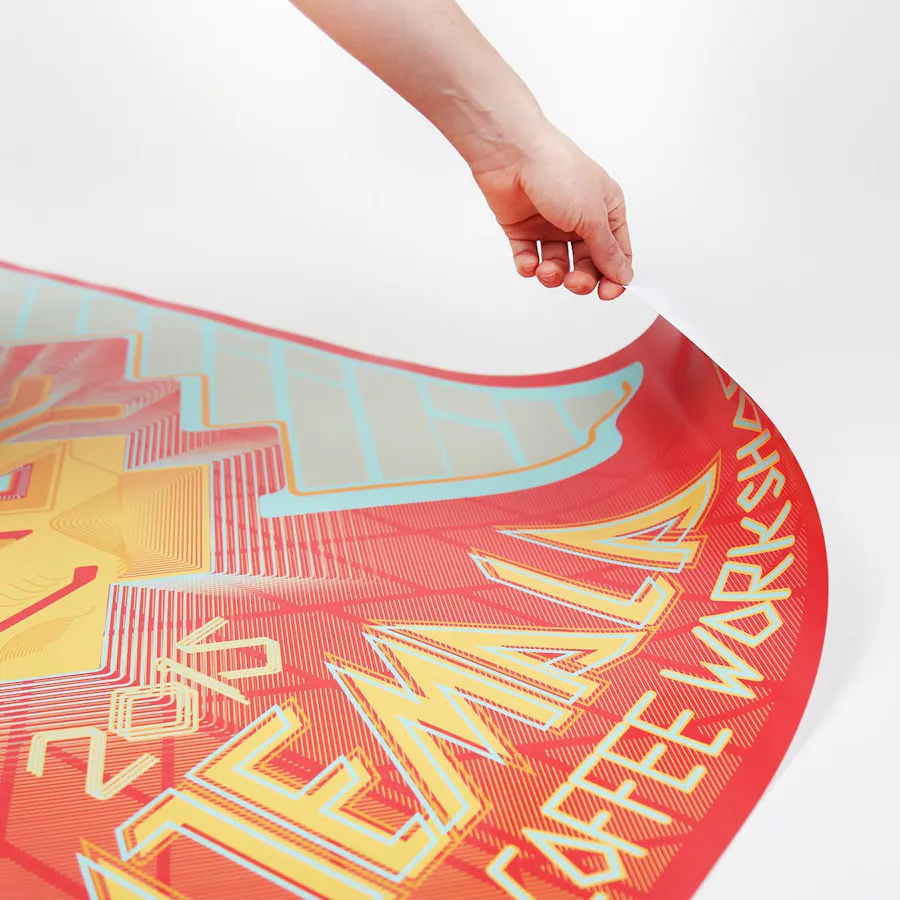 A hand pulling up the corner of a custom poster with a bright orange, yellow and light teal design.
