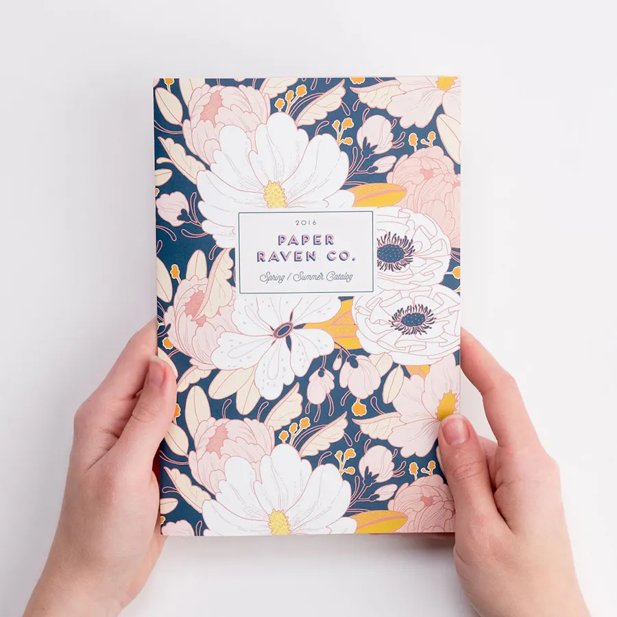 Two hands holding a printed brand lookbook with a floral design.