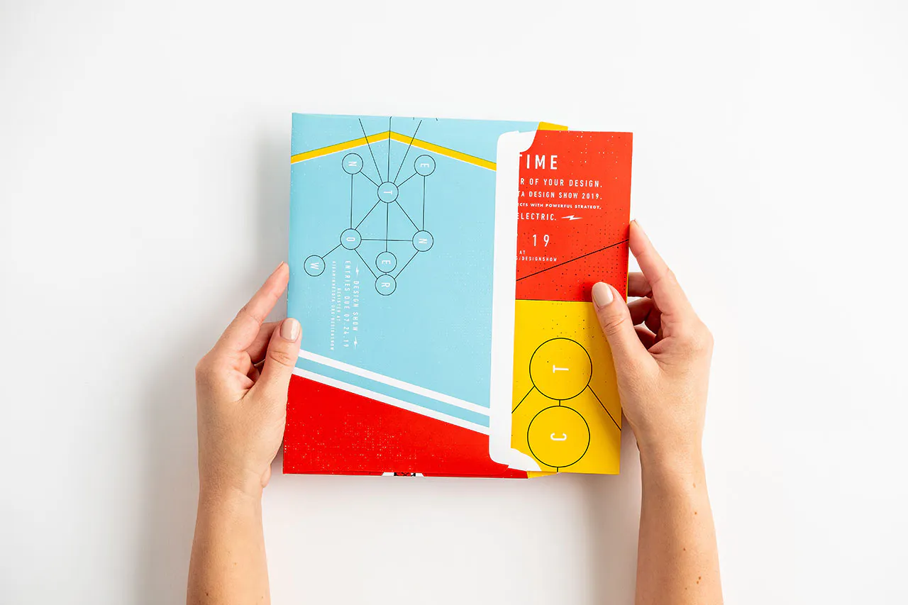 Two hands pulling a folded direct mail poster out of its envelope with a blue, red and yellow design.