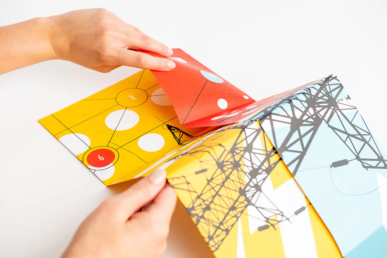 Two hands unfolding a direct mail poster with a yellow, white, red, black and blue design.