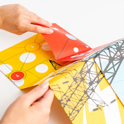 Two hands unfolding a direct mail poster with a yellow, white, red, black and blue design.