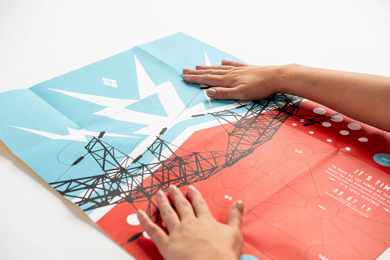 Two hands laying on an unfolded direct mail poster with a blue, red, black and white design.