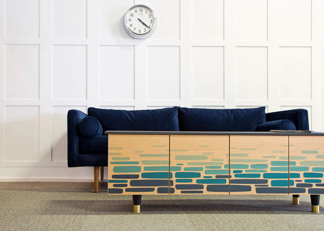 A coffeetable designed with custom art in shades of blue sitting in front of a navy couch with a clock hanging above it.