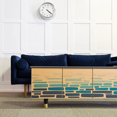 A coffeetable designed with custom art in shades of blue sitting in front of a navy couch with a clock hanging above it.
