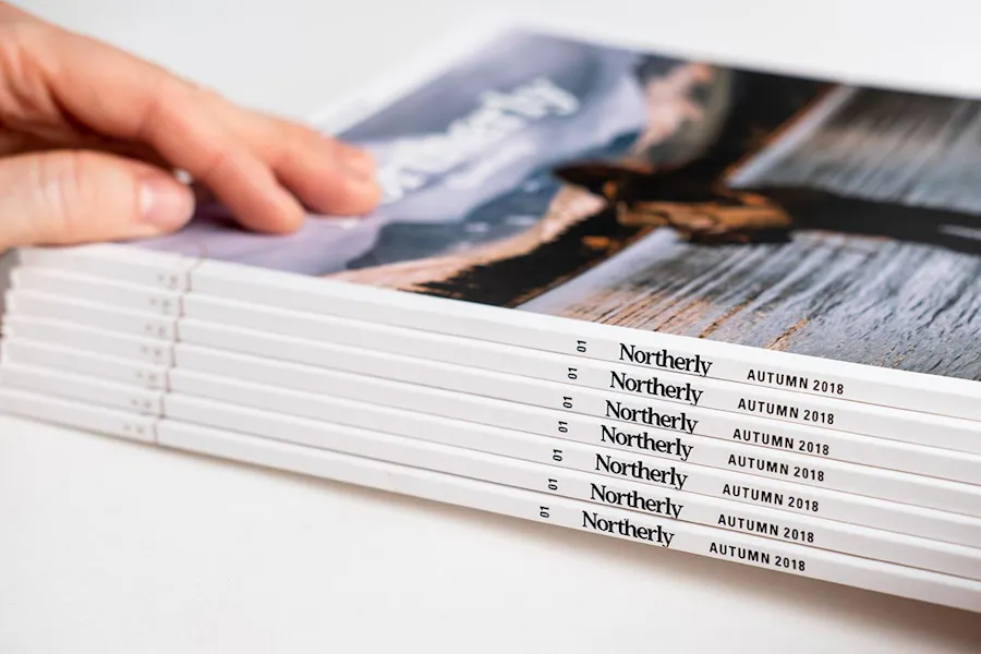 A hand on top of a stack of perfect bound booklets with Northerly on the spines.