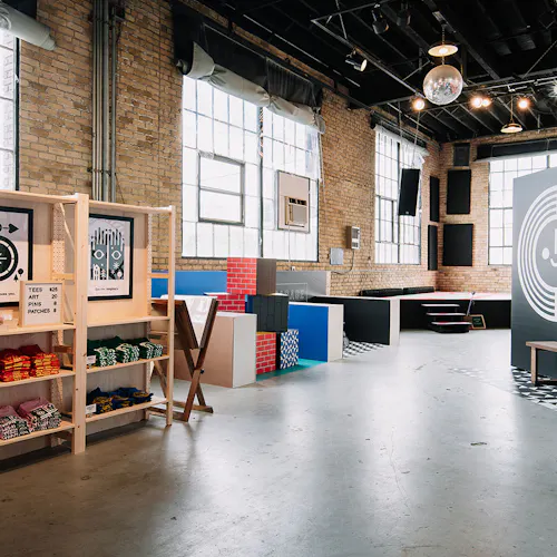 A warehouse space with brick walls, a stage in the corner, blocks with custom decals on the sides and a T-shirt display.