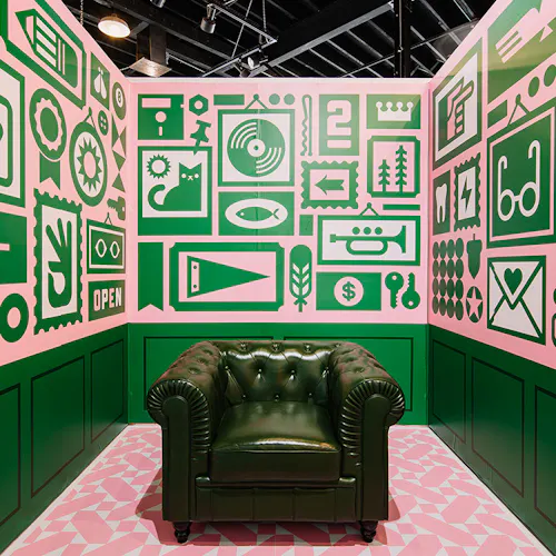 A green club chair in the middle of a display with custom wall decals printed with pink and green designs surrounding it.