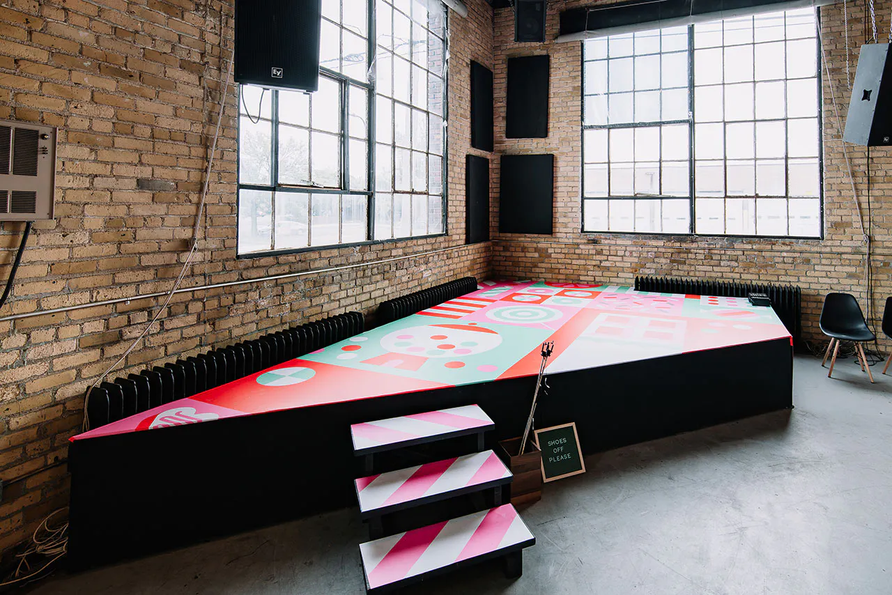 A stage in a warehouse with bright pink, red and teal decals on the steps and stage floor.