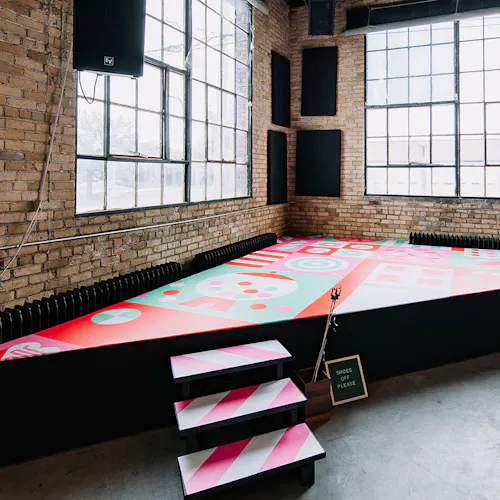 A stage in a warehouse with bright pink, red and teal decals on the steps and stage floor.