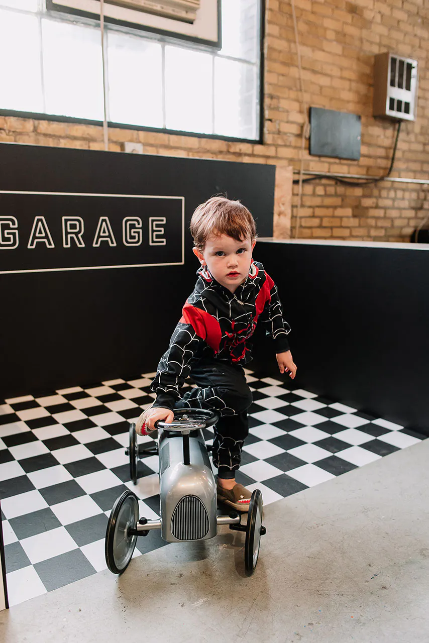 A little boy wearing a black and red hoodie playing with a gray toy tractor on a black and white checkered floor.