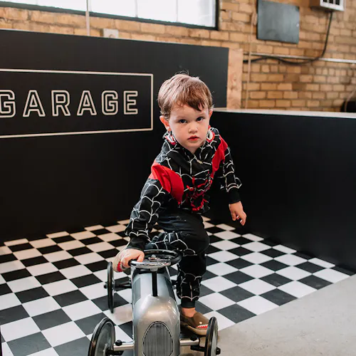 A little boy wearing a black and red hoodie playing with a gray toy tractor on a black and white checkered floor.