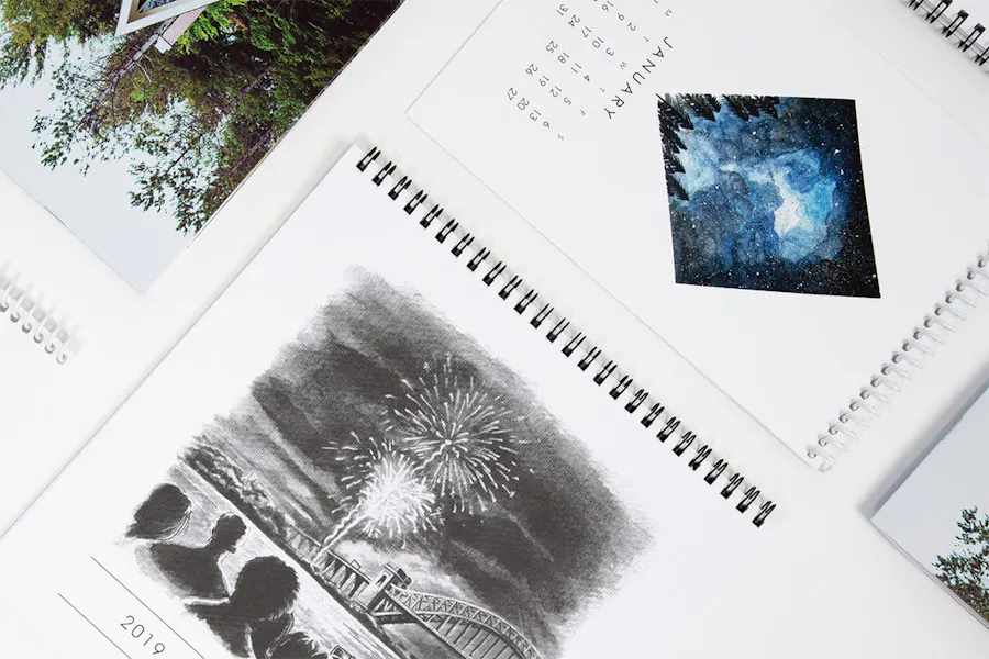 Six spiral bound calendars laid out in rows with custom artwork, including fireworks, a cabin and space.