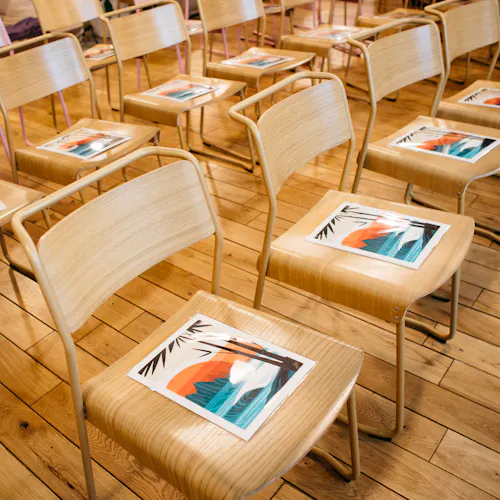Wooden chairs lined up in rows with a custom art print laying on the seat of each one.