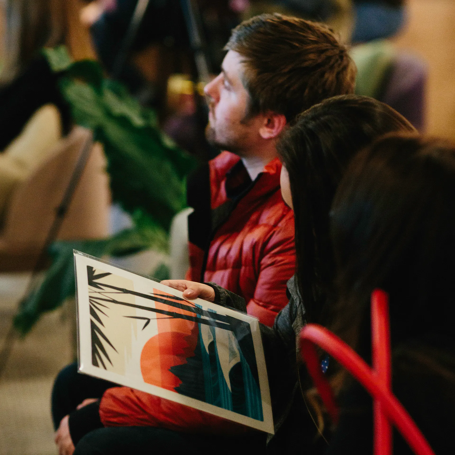 People sitting in an audience listening to presenters and holding custom artwork in their laps.