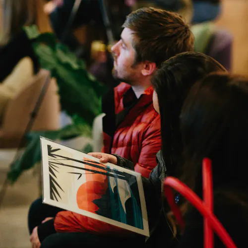 People sitting in an audience listening to presenters and holding custom artwork in their laps.