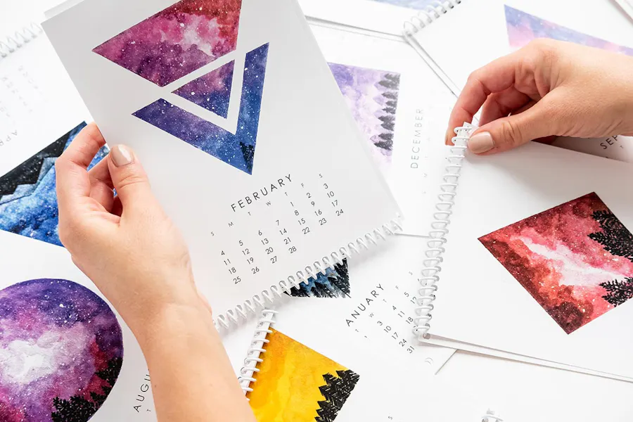 Two hands holding custom printed calendars with a spiral binding and images of galaxies.