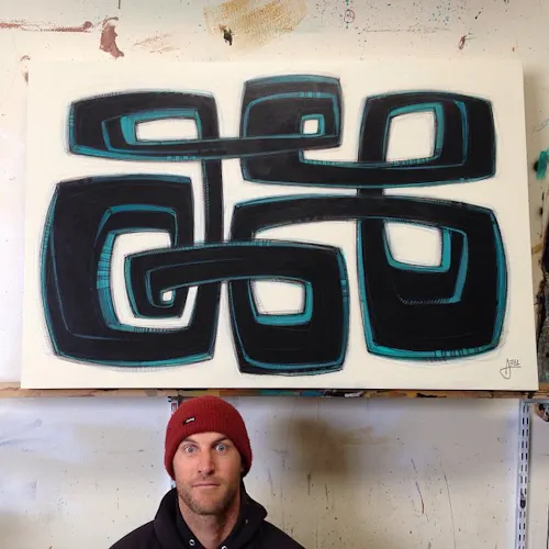 A man wearing a hoodie and a stocking cap standing in front of a custom art print with a design in black and blue.