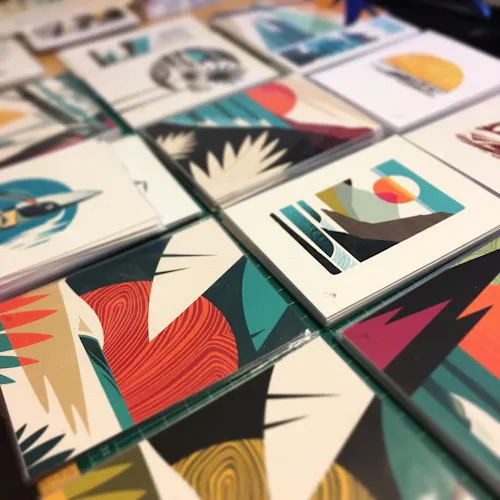 Custom art prints laid out in rows on a table with abstract ocean-inspired designs in shades of teal, black, red and orange.