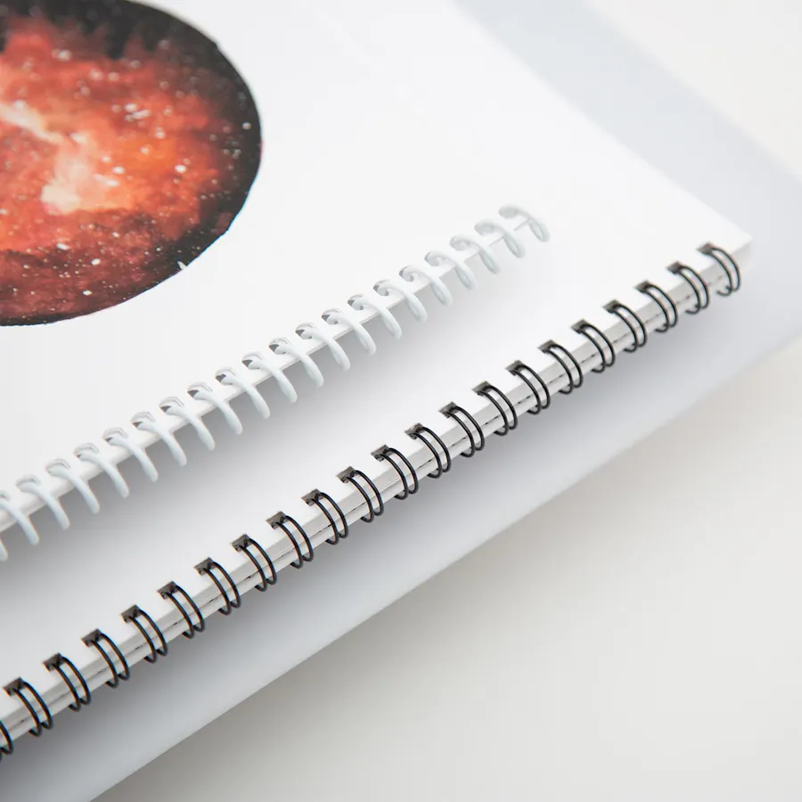 One spiral bound calendar printed with a red space design stacked on top of a wire coil calendar.