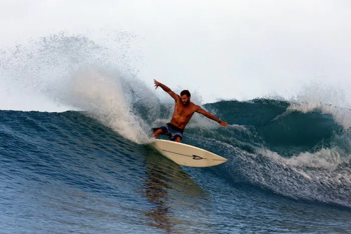 A man wearing navy blue shorts surfing in the ocean on a white surfboard.