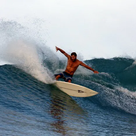 A man wearing navy blue shorts surfing in the ocean on a white surfboard.