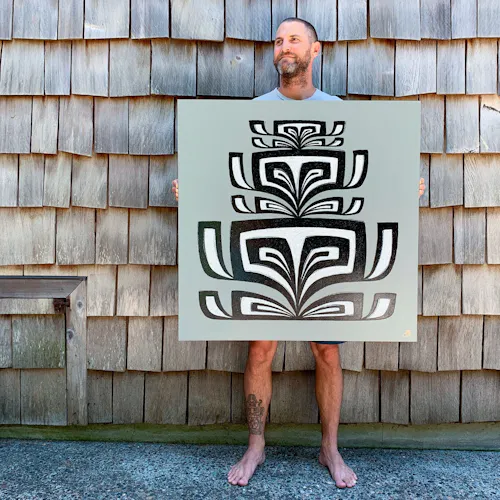 A man standing in front of a building with wooden siding holding a custom art print with an abstract design.