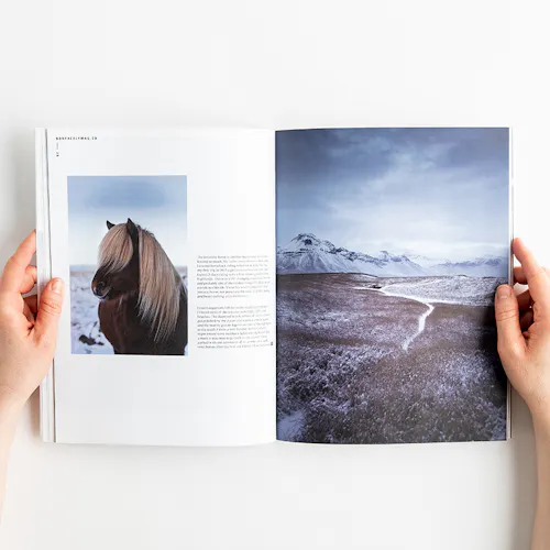 Two hands holding open a photography magazine to images of a horse and a mountain landscape in winter.