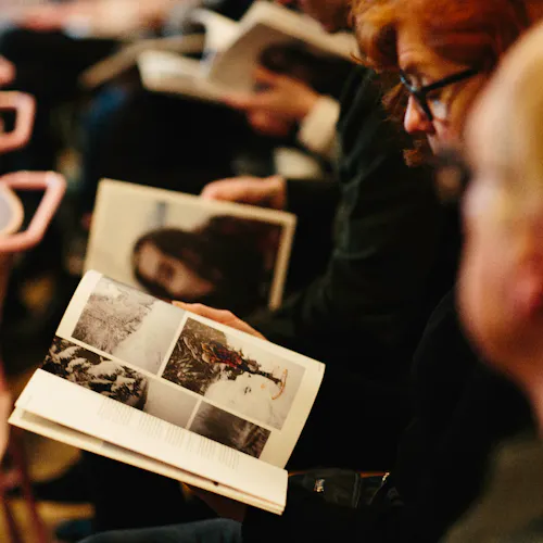 People sitting in rows of chairs during a presentation and flipping through a Northerly magazine.