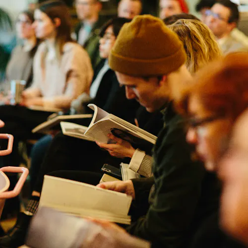 An audience sitting in rows of chairs and flipping through a Northerly photography magazine during a presentation.