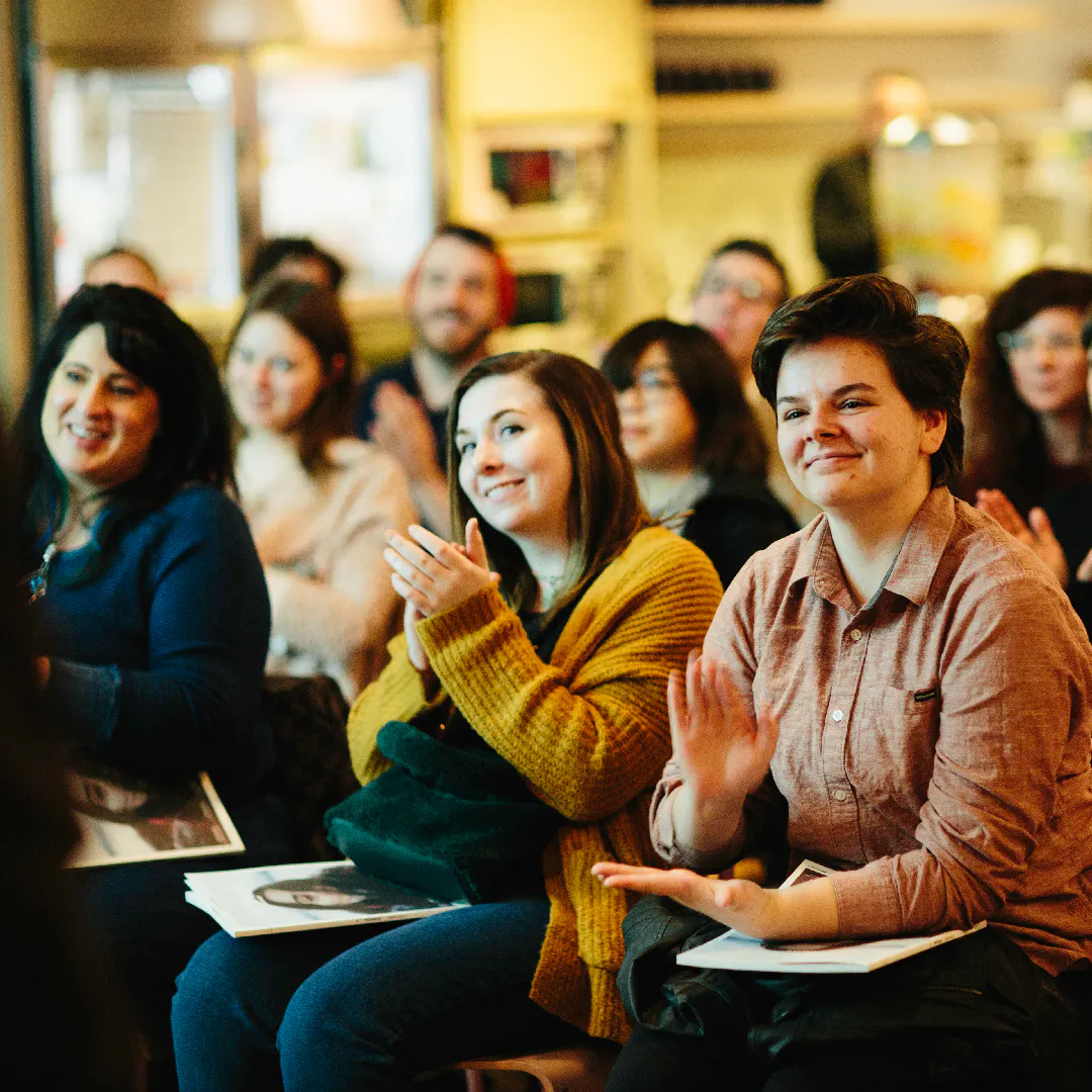 An audience of people smiling and sitting on chairs with a custom printed magazine in their laps.