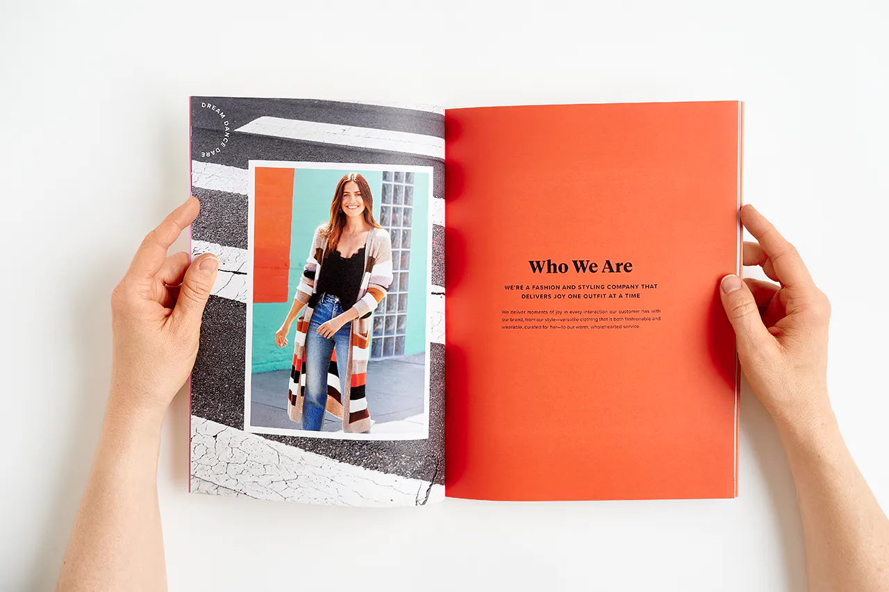 An Evereve brand book laying open to a woman smiling in a striped cardigan and Who We Are in black.