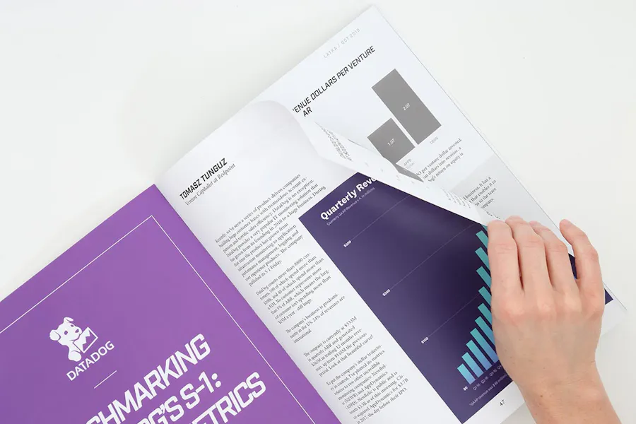 A direct mail magazine laying open to a purple and blue bar chart with a hand turning the page.