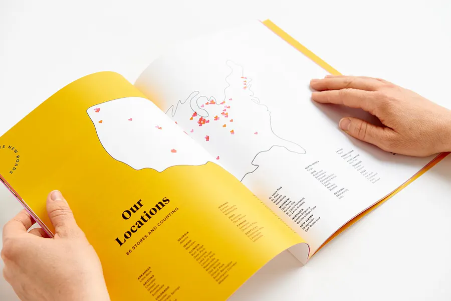 Two hands holding an Evereve brand book open to store location information in a yellow design.