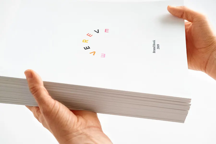 Two hands holding a stack of an Evereve brand book with a perfect binding.