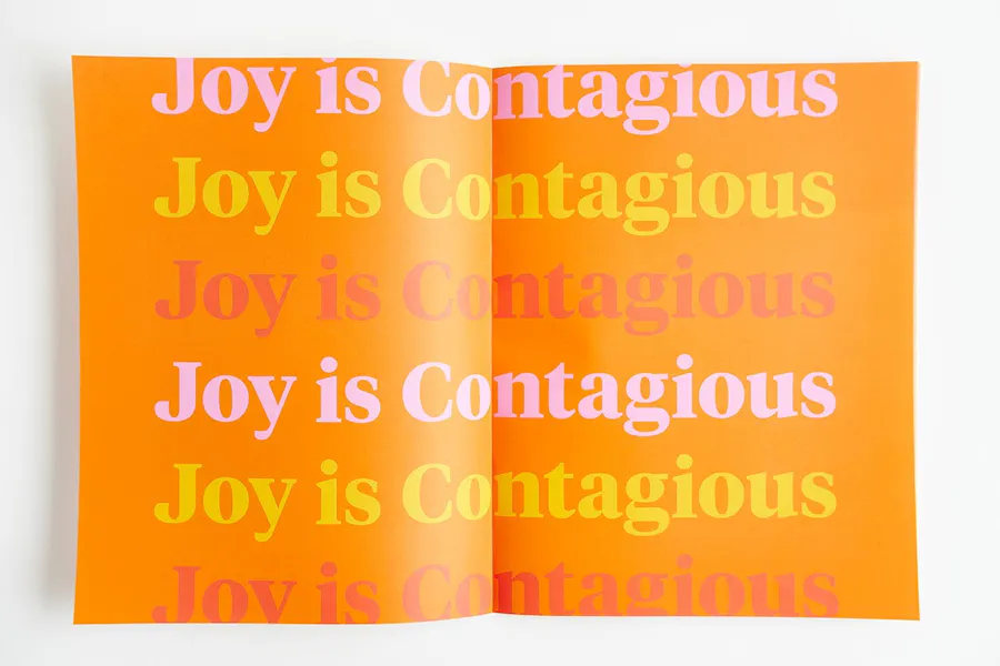 A custom booklet printed as a brand book laying open to pages with an orange background and Joy is Contagious.
