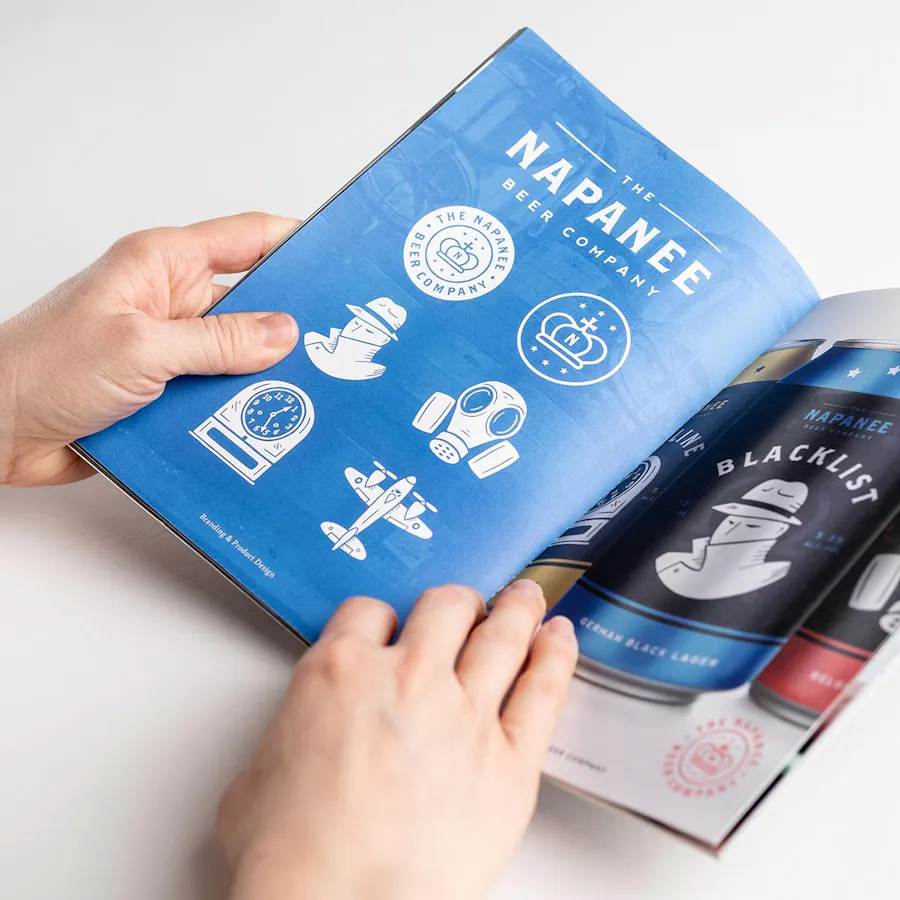 Two hands holding open a booklet with The Napanee Beer Company on the left page and beer cans on the right page.