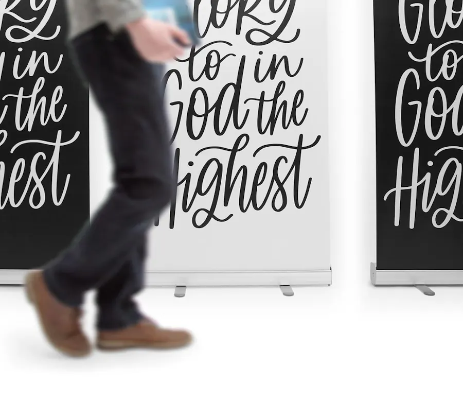 A person walking back three custom banners printed with God in the Highest in swirling letters.