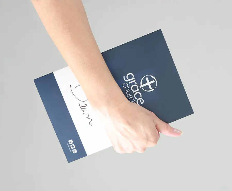 A hand holding a church booklet printed with grace church on the front.