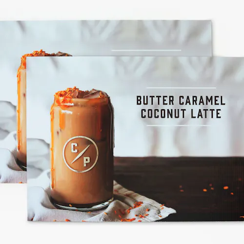 A corrugated plastic sign printed with Butter Caramel Coconut Latte next to an iced coffee on a cloth napkin on a table.