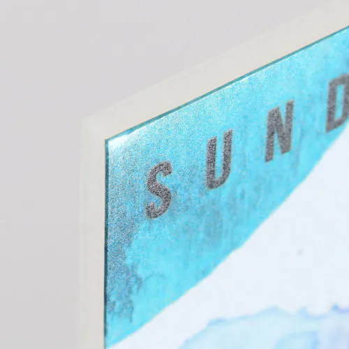 The corner of a foamcore sign custom printed with a blue sky and clouds design and Sunday at the top.