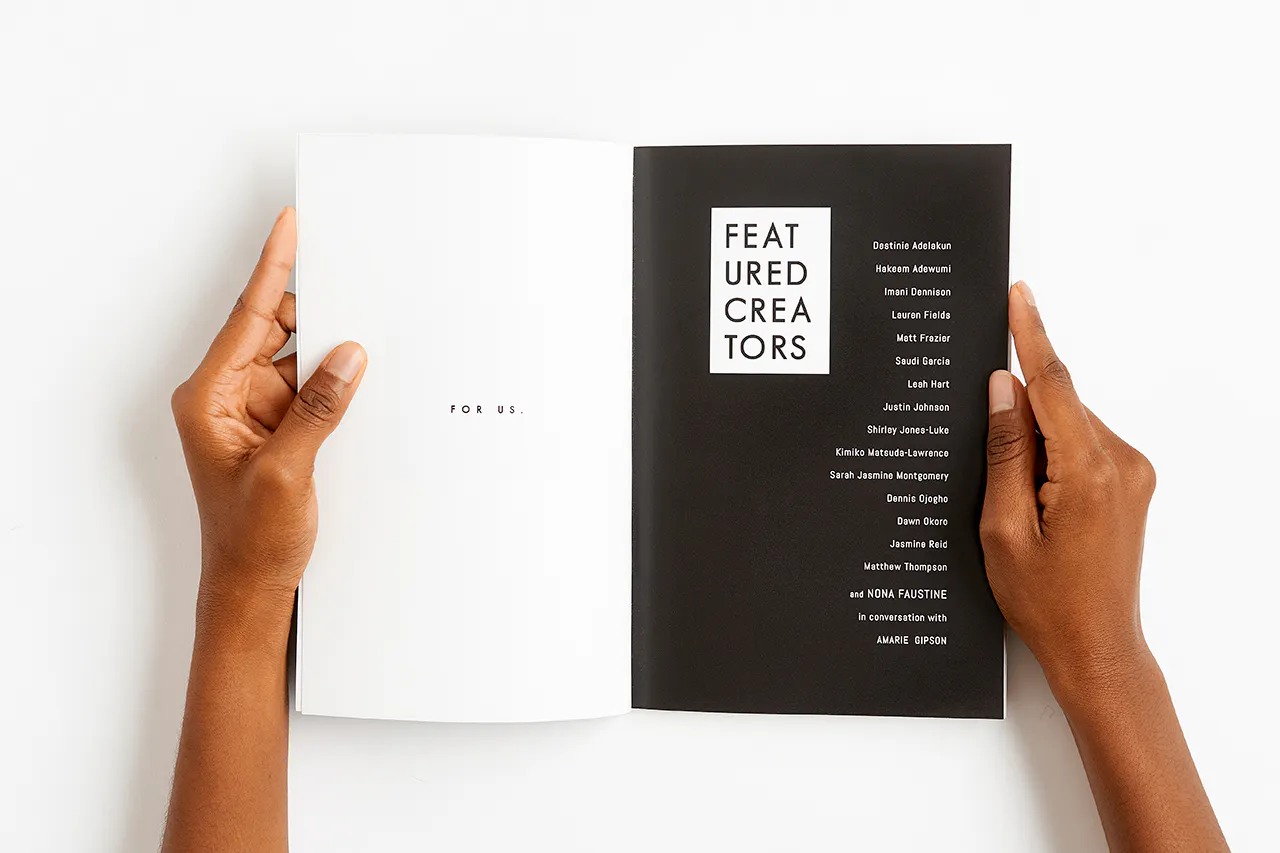 Two hands holding a magazine open to a black and white design and printed with For Us and Featured Creators.