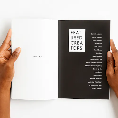 Two hands holding a magazine open to a black and white design and printed with For Us and Featured Creators.
