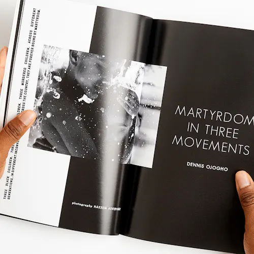 Two hands holding a magazine open to a black and white image of two people hugging and being splashed with water.