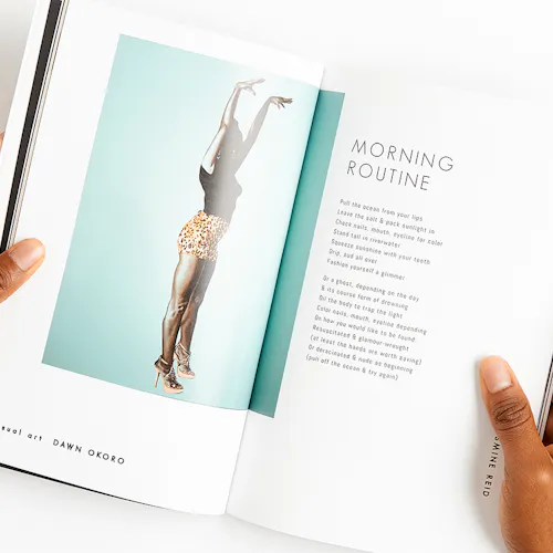 Two hands holding a magazine open to a woman wearing heels, shorts and a T-shirt raising her arms above her head.