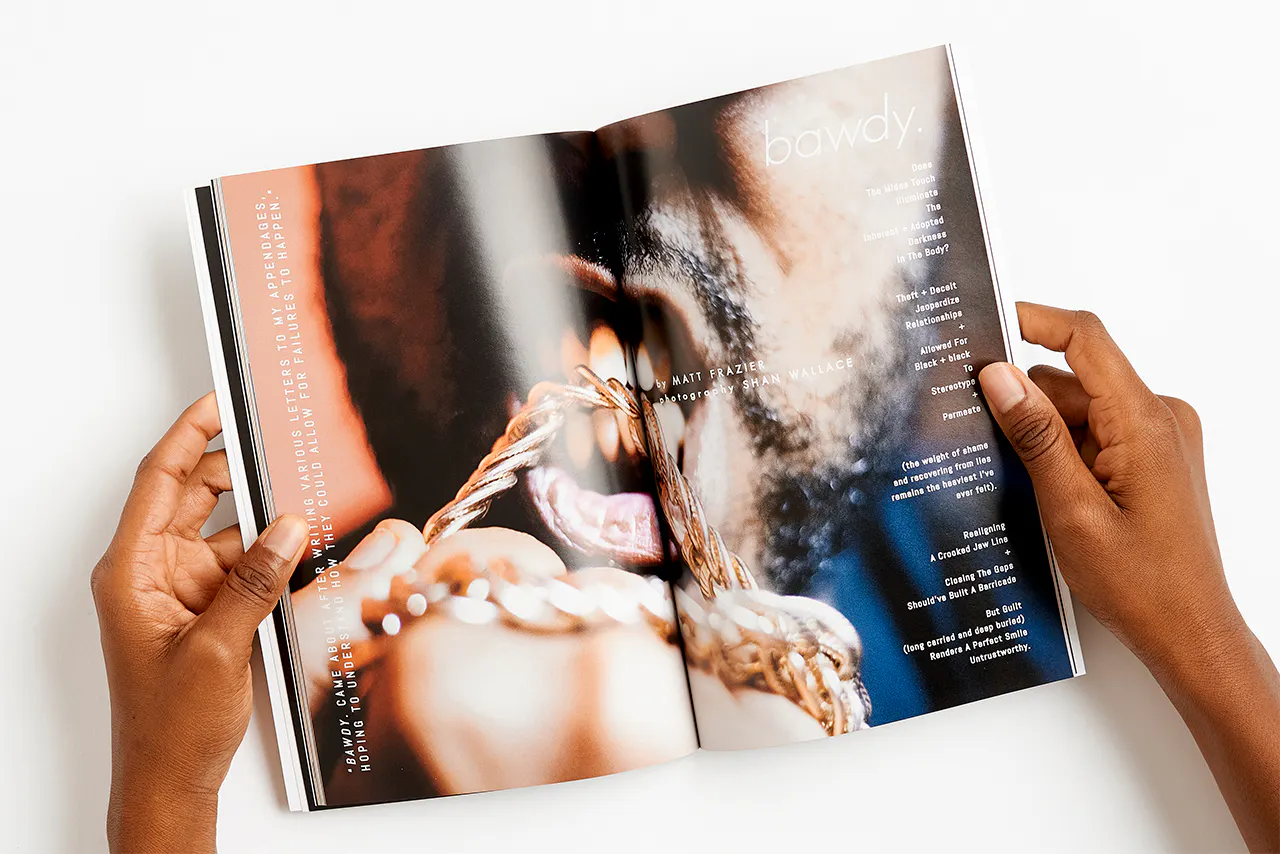 Two hands holding a magazine open to a close-up of a man biting a gold chain.