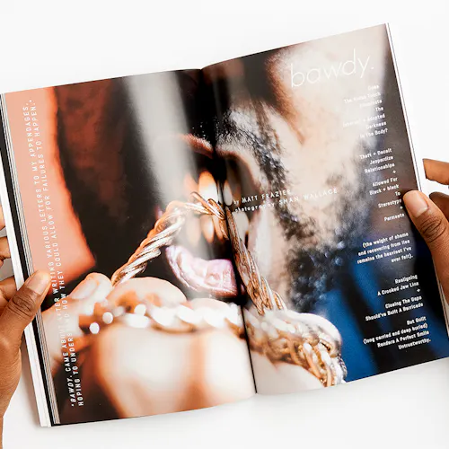 Two hands holding a magazine open to a close-up of a man biting a gold chain.