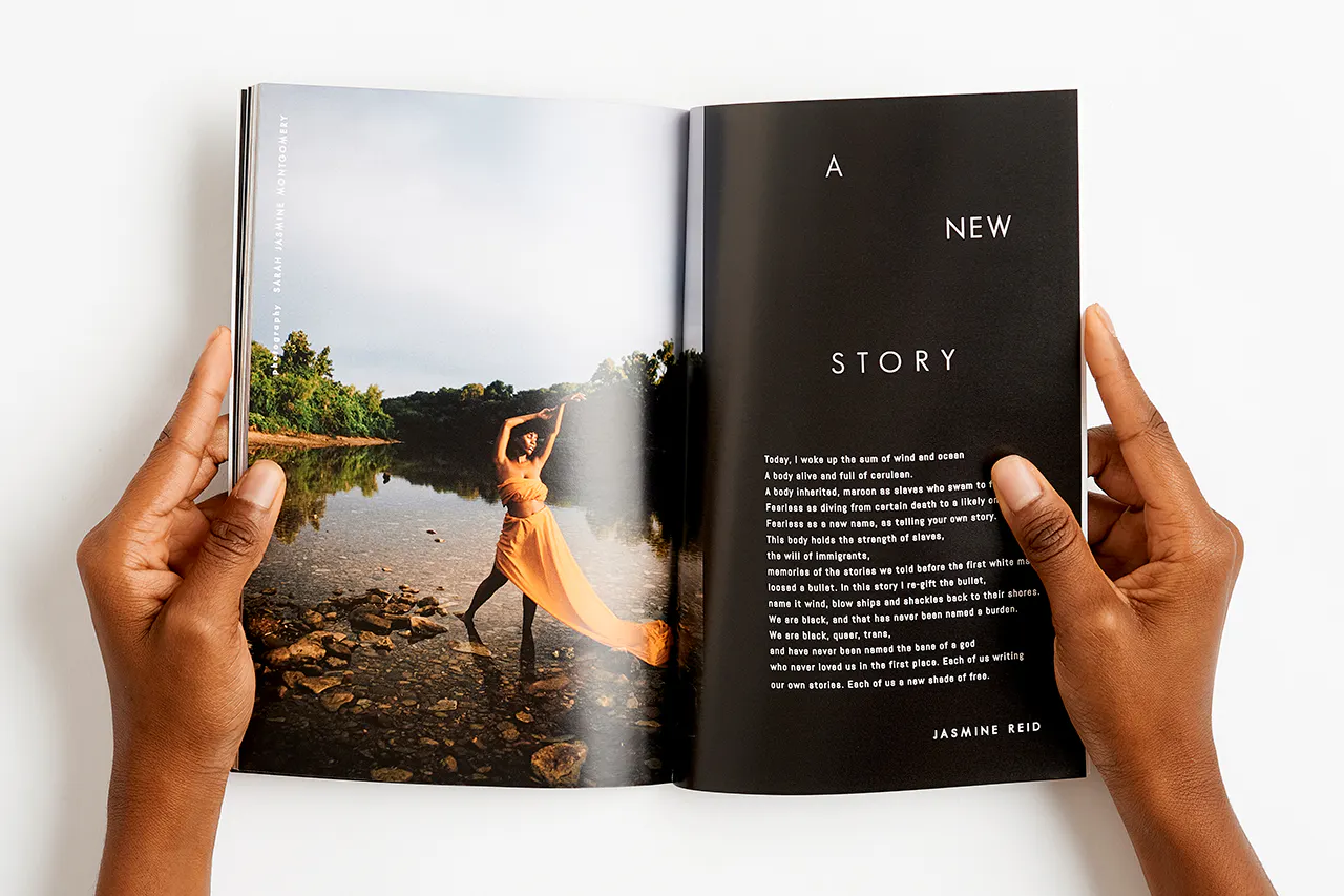 Two hands holding a magazine open to a woman in a yellow dress standing in water.
