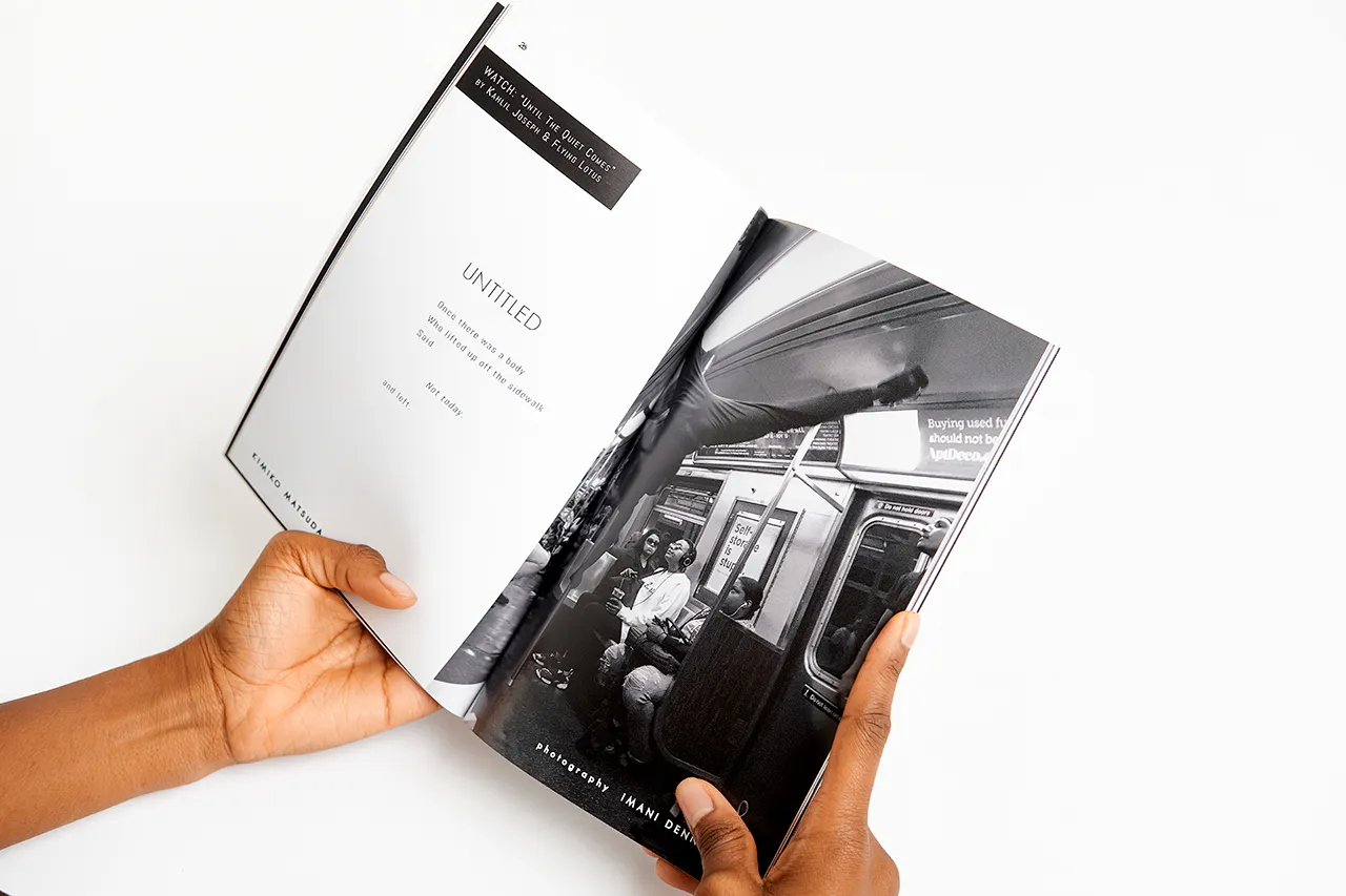 Two hands holding a magazine open to a black and white images of people in a subway car.