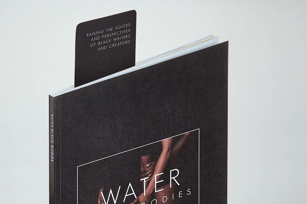 A bookmark sticking out of a literary magazine printed with Water Black Bodies on the black cover.